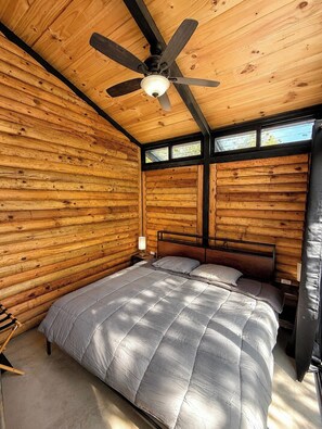 A wooden cabin bedroom with a bed, a ceiling fan, and a window. - VILLA AMADA. Cabaña Alba (Santiago)