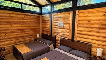 Une chambre de style cabane avec deux lits, un ventilateur de plafond et de grandes fenêtres.