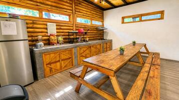 Una cocina rústica con paredes de madera, un refrigerador de acero inoxidable, una mesa de madera y un banco.
