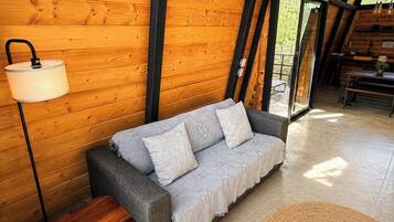 Una habitación acogedora con techo de madera, un sofá gris con cojines estampados, un pequeño cofre de madera y una alfombra tejida.