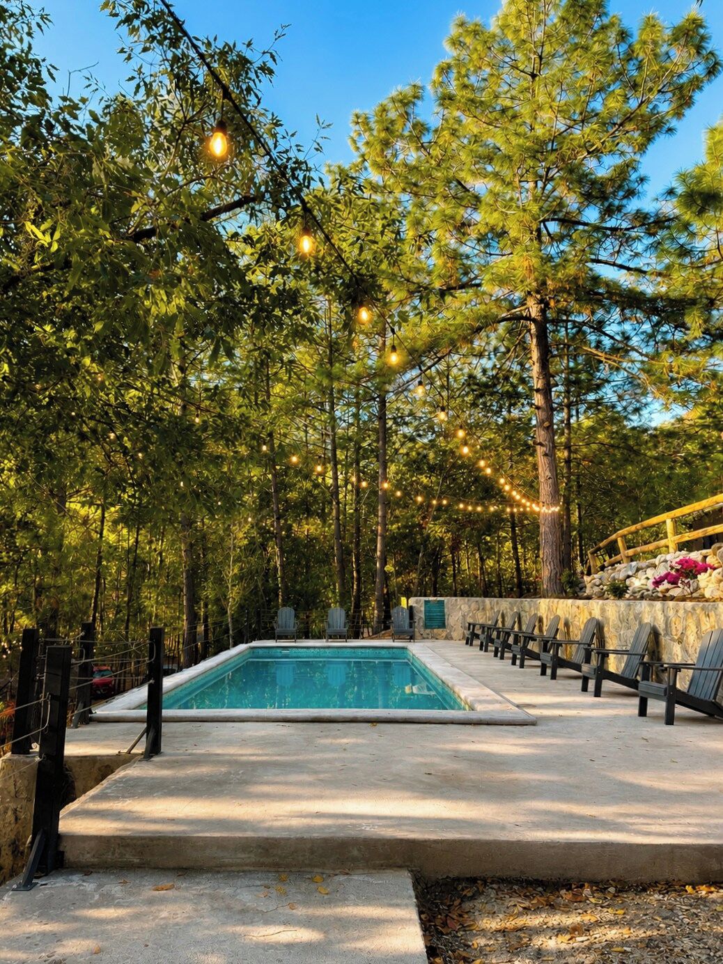 Ein Schwimmbecken mit Steinmauer und Stühlen, umgeben von Bäumen und Lichterketten.