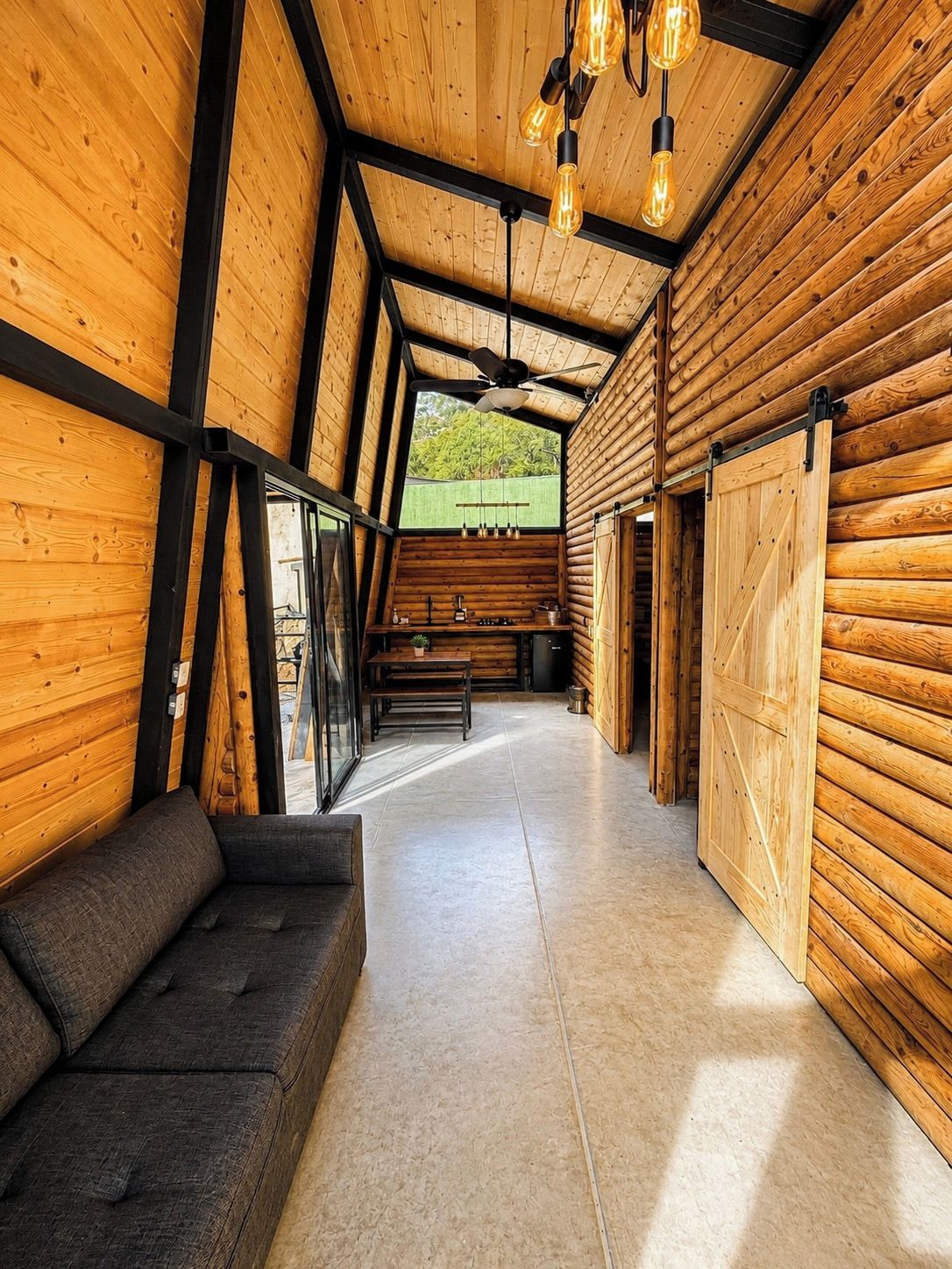 Un interno moderno con pareti in legno, soffitto nero, un divano, un tavolo da pranzo e vista dalla finestra.