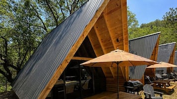 Una cabaña de madera con techo inclinado, mobiliario exterior y una parrilla.