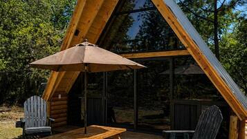 Eine dreieckige Holzjagdhütte mit Picknicktisch und -stühlen, einem Grill und einer überdachten Sitzgelegenheit.