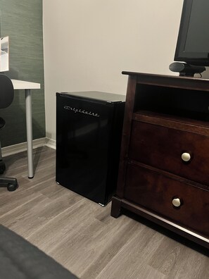 A compact black refrigerator with the brand name visible, a wooden dresser with drawers, and a white desk with a chair. - Modern Gulfport Retreat. Stylish 1 BR, Full Kitchen, Patio & Private Driveway (Gulfport)