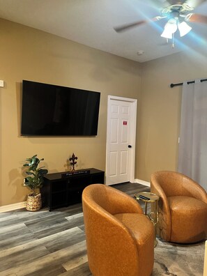 A living room with a flat-screen TV, a door, two leather armchairs, a small side table, and a ceiling fan. - Modern Gulfport Retreat. Stylish 1 BR, Full Kitchen, Patio & Private Driveway (Gulfport)