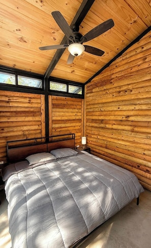 Un dormitorio de cabaña de madera con una cama, un ventilador de techo y una ventana.