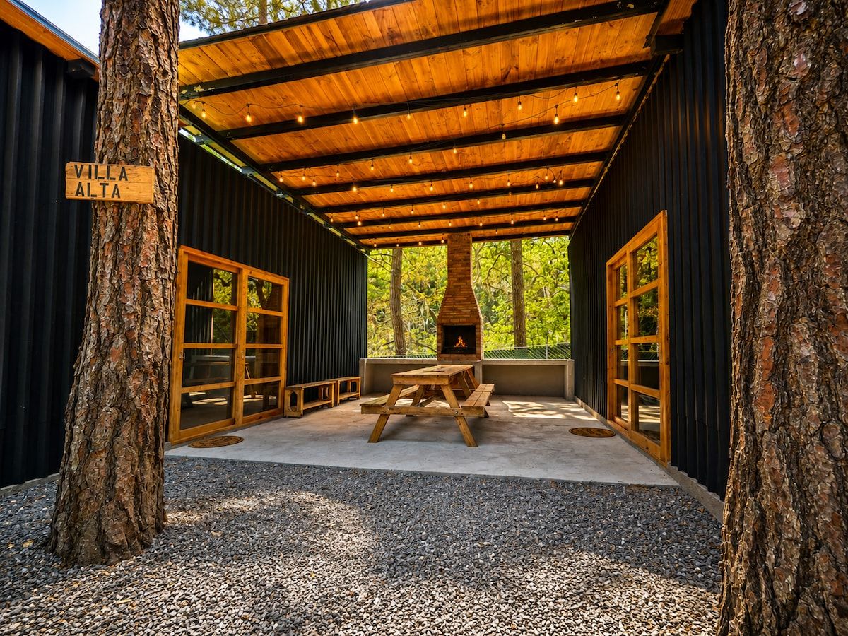 A covered outdoor seating area with a wood-burning stove, benches, and a sign reading 'Villa Alta'.