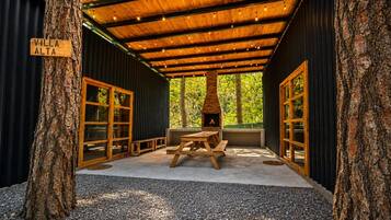 A covered outdoor seating area with a wood-burning stove, benches, and a sign reading 'Villa Alta'.