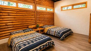 A log cabin bedroom with two beds, wooden walls, a ceiling fan, and windows.