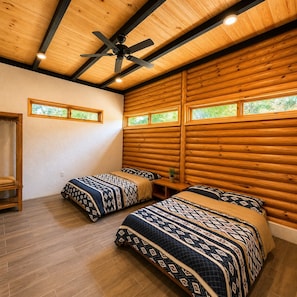 A log cabin-style room with two beds, a ceiling fan, and windows.