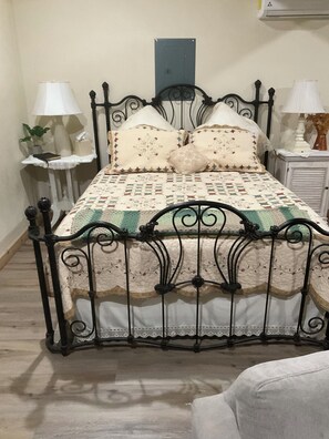 Un lit avec un cadre en métal, une courtepointe à motifs et deux tables de chevet avec des lampes.
