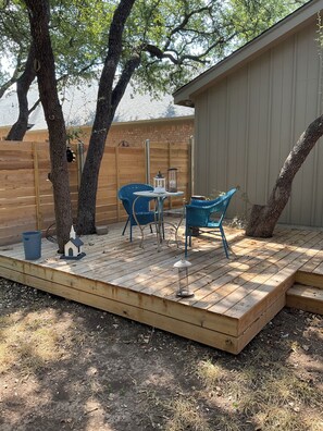 Eine Holzterrasse mit Tisch und Stühlen, umgeben von Bäumen und einem Holzzaun.