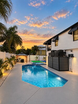 A swimming pool with a patio area, a barbecue setup, and a view of a sunset. - Siesta Key Beach House | Arcade, Pickleball, Pool (Sarasota)