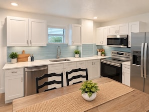 A modern kitchen with white cabinets, stainless steel appliances, and a wooden dining table. - Siesta Key Beach House | Arcade, Pickleball, Pool (Sarasota)