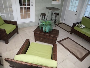 A room with wicker furniture, a green cushioned sofa, a small table, and a potted plant. - Spacious 4-Bedroom Retreat in peaceful Roswell (Roswell)