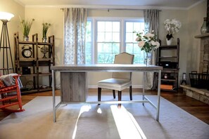 Una habitación con una mesa de comedor, una silla, una lámpara, un sillón mecedora y una ventana con cortinas.