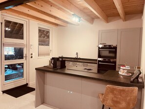 A modern kitchen with a central island, built-in oven, and a window with blinds.