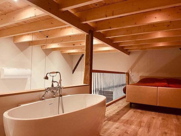 A modern bathroom with a freestanding bathtub, a large mirror, and a wooden ceiling.