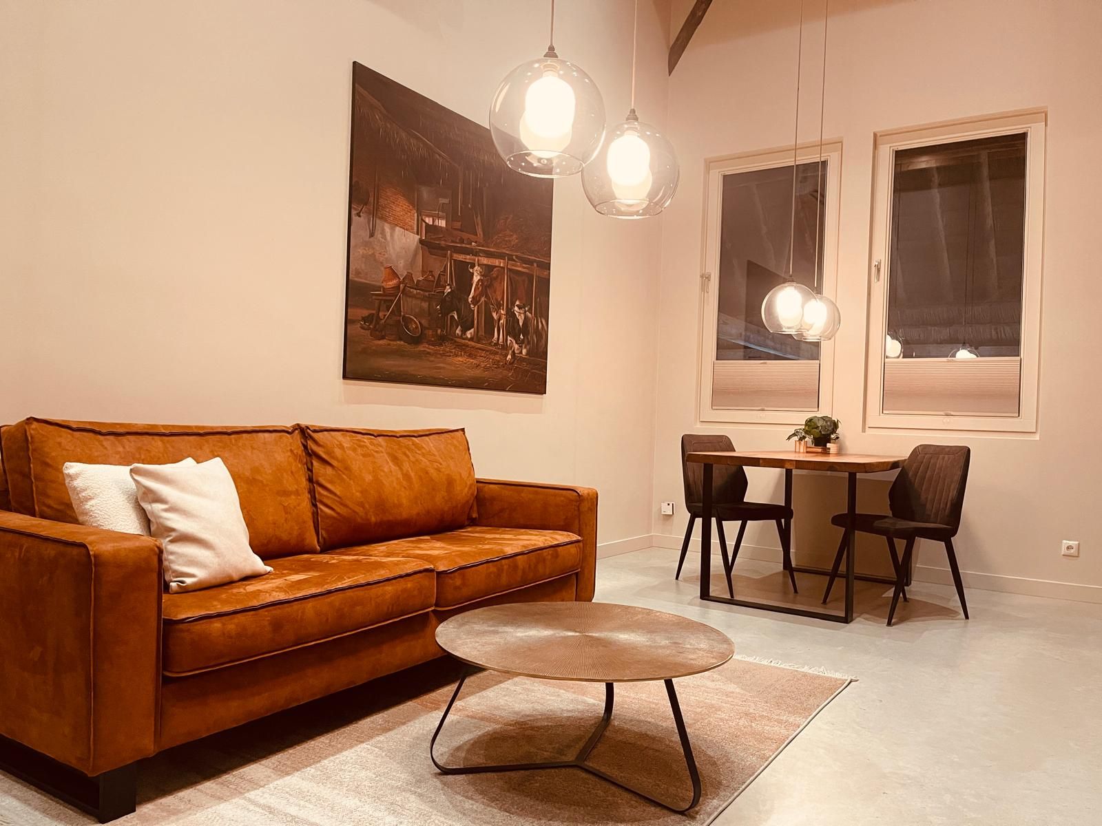Ein Wohnzimmer mit einem braunen Ledersofa, einem runden Couchtisch und einem Essbereich mit kleinem Tisch und Stühlen.