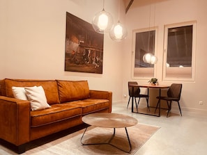 A living room with a brown leather sofa, a round coffee table, and a dining area with a small table and chairs.