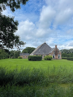 Une grande maison avec un toit en pente, entourée d’une pelouse bien entretenue et d’une végétation luxuriante.