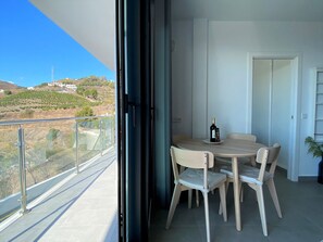 A balcony with a glass railing, a dining table with chairs, and a bottle of wine on the table. - Apartment in Nerja With Panoramic Sea Views (Nerja)