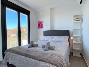 A bedroom with a large bed, a nightstand, a bedside table, a window with a view, and a wall-mounted shelf. - Apartment in Nerja With Panoramic Sea Views (Nerja)