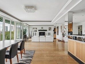 A modern living room with a white sofa, a dining area with a black table and chairs, and a kitchen with wooden cabinets. - Passy - Pdt. Kennedy 2 bd by B'Your Home (Paris)