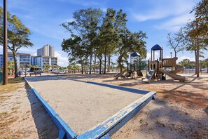 Ein Spielplatz mit Sand, einem blau gestrichenen Spielbereich und Bäumen.