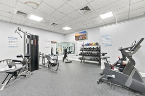 Uma academia com diversos equipamentos de exercícios, incluindo esteira, aparelhos de musculação e um suporte com halteres.