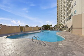 A swimming pool with a curved design, surrounded by a tiled deck and a beige building. - Sun and Splash Myrtle Beach Resort Condo (Myrtle Beach)