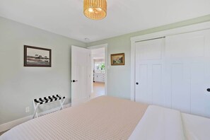 A bedroom with a bed, a door, and a hallway leading to a bathroom. - Blue Rocks Ocean Bliss for 10 (South Shore NS)