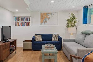 A living room with a blue sofa, a grey sofa, a wooden TV stand, and a bookshelf. - Blue Rocks Ocean Bliss for 10 (South Shore NS)