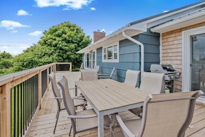 A deck with a table and chairs, a grill, and a view of a tree and house. - Blue Rocks Ocean Bliss for 10 (South Shore NS)