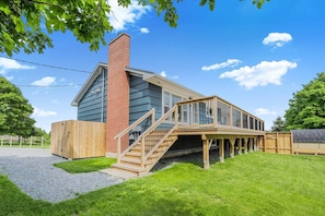 A two-story house with a wooden deck, a brick chimney, and a gravel driveway. - Blue Rocks Ocean Bliss for 10 (South Shore NS)