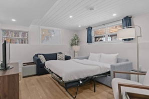 A compact room with a bed, a desk, a bookshelf, a map on the wall, and a window with curtains. - Blue Rocks Ocean Bliss for 10 (South Shore NS)