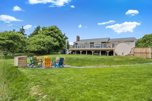 A house with a large deck, a garage, and a grassy yard with outdoor furniture. - Blue Rocks Ocean Bliss for 10 (South Shore NS)