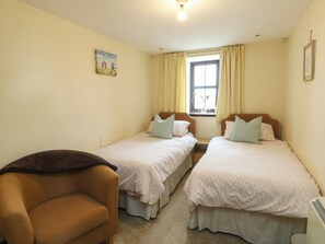 A bedroom with two single beds, a chair, a window with curtains, and a painting on the wall. - Getws (Ty Croes)