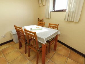 A dining area with a table and four chairs, a window with curtains, and a tiled floor. - Getws (Ty Croes)