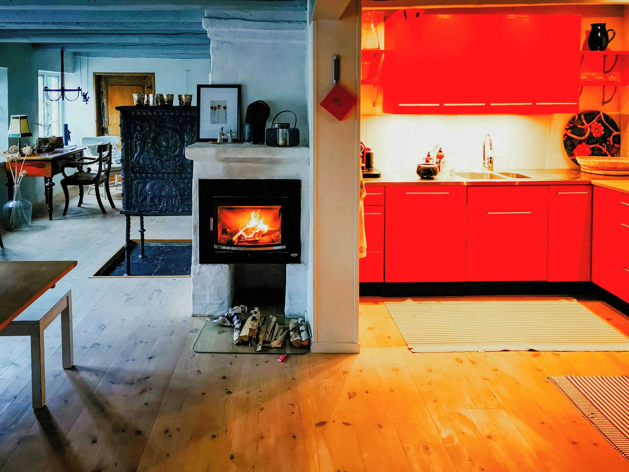 Una sala de estar moderna con chimenea, un comedor y una cocina con armarios rojos.