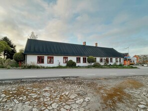 A two-story white building with a dark roof, multiple windows with red frames, and a cobblestone driveway.