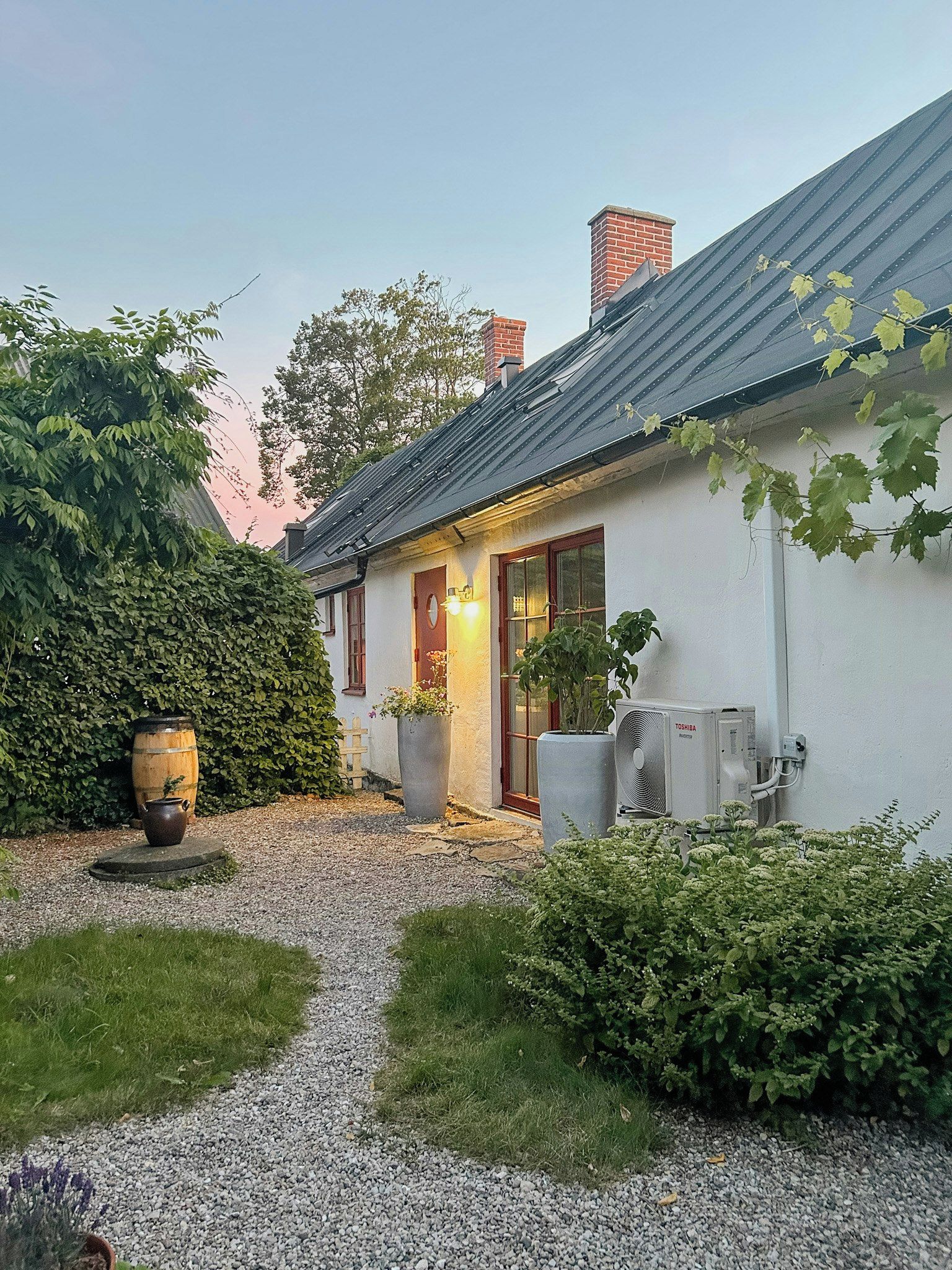 A house with a gravel driveway, a wooden barrel, and a large air conditioning unit.