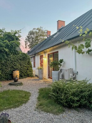 A house with a gravel driveway, a wooden barrel, and a large air conditioning unit. - Charming Skåne Cottage in the Heart of Österlen (Simrishamn)