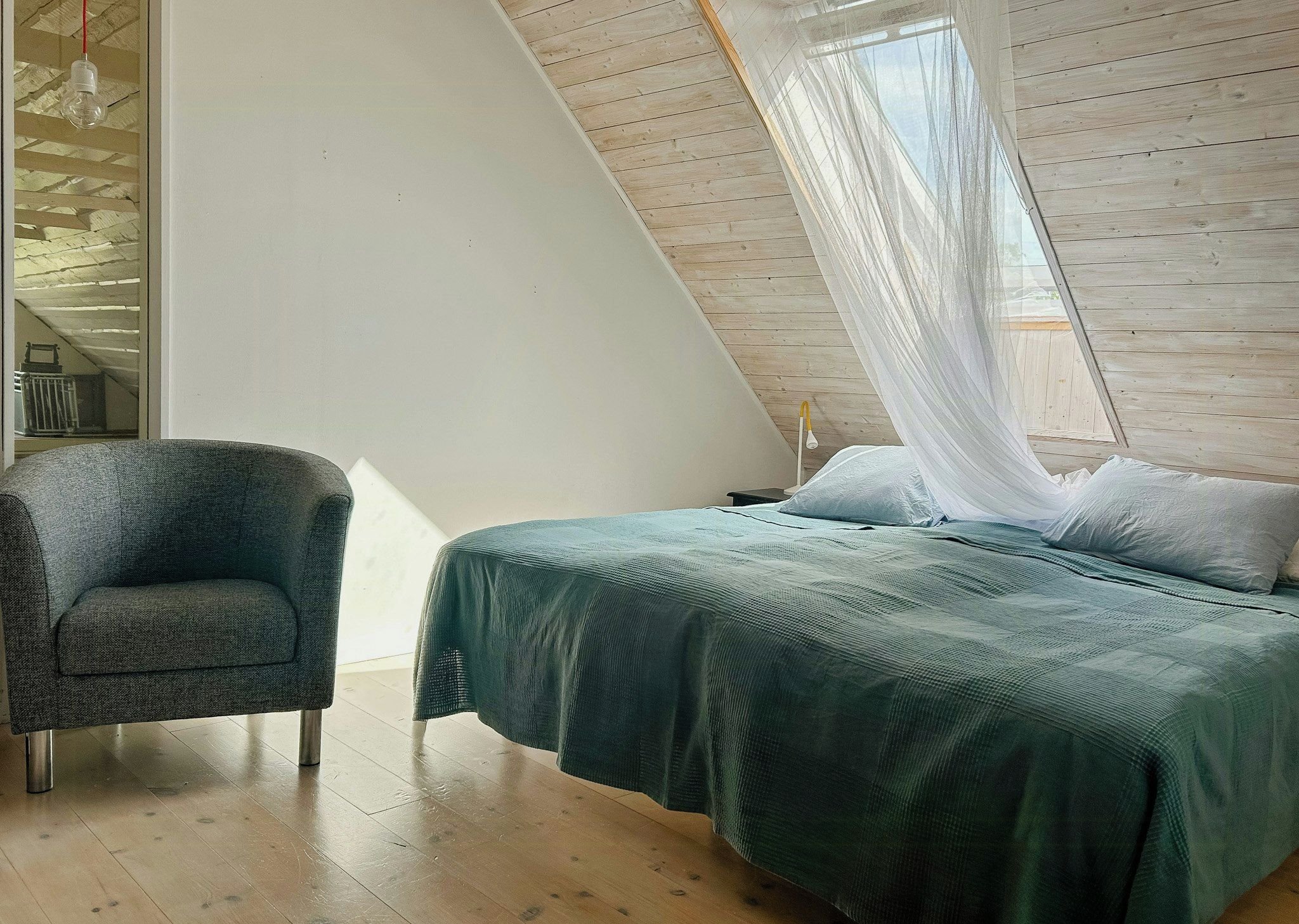 Une chambre à coucher avec un lit, une chaise et une fenêtre ornée d’un rideau léger.