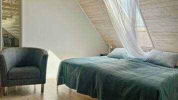 Une chambre à coucher avec un lit, une chaise et une fenêtre ornée d’un rideau léger.