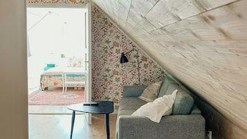 An attic room with a sloped ceiling, a grey sofa, a small table, and a patterned wallpaper.