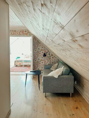 An attic room with a sloped ceiling, a grey sofa, a small table, and a patterned wallpaper. - Charming Skåne Cottage in the Heart of Österlen (Simrishamn)