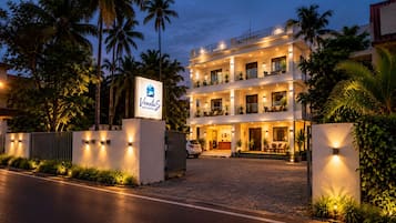 Un hotel de varios pisos con área de recepción, asientos al aire libre y una entrada bien iluminada.