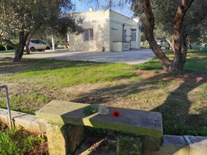 A park with a concrete bench, a building in the background, and a car parked on the street. - Villa 'Mios' with Private Terrace, Wi-Fi and Air Conditioning (Muro Leccese)